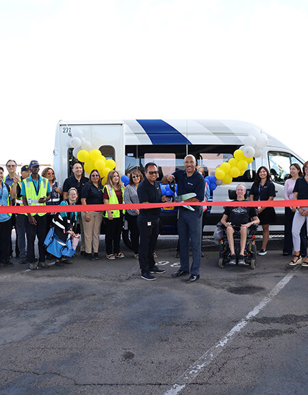 Ribbon cutting of Sun Van vehicles, outside, with three vehicles lined up and lots of people in front holding the ribbon in celebration.